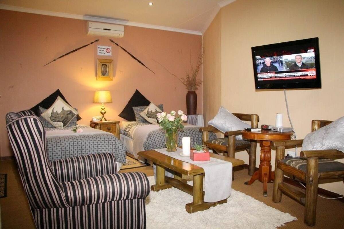 Ein gemütliches Zimmer mit Bett, einem gestreiften Ohrensessel, einem Holztisch und einem Fernseher, der eine Nachrichtensendung zeigt.