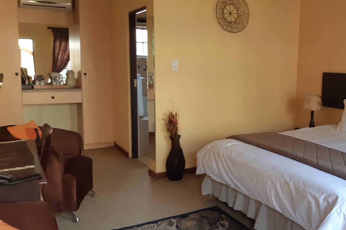 Ein Hotelzimmer mit einem Bett, einem Schreibtisch, einem Stuhl, einer Vase mit Trockenblumen und einem Bild an der Wand.