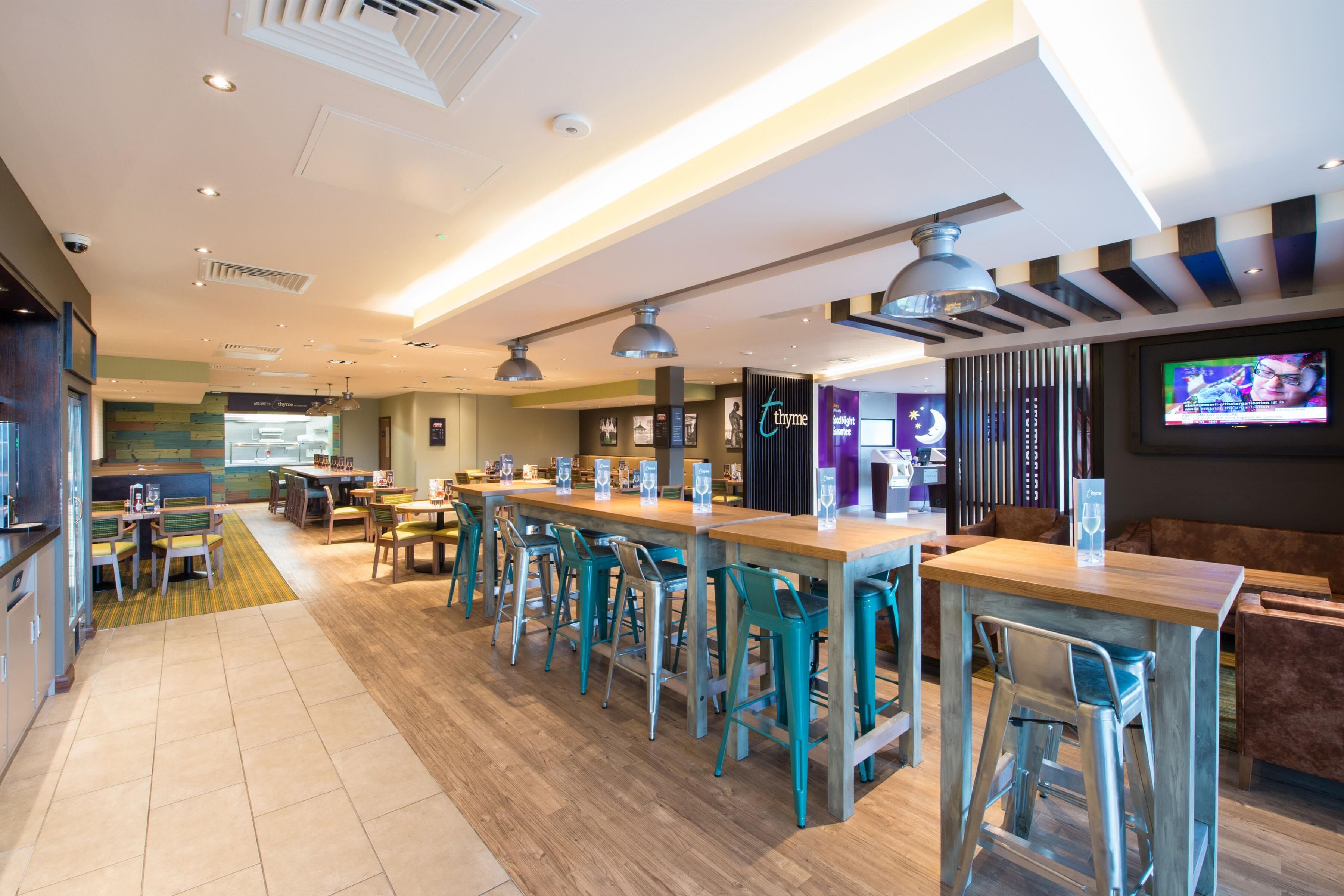 Uma área de bar moderna com mesas altas e banquetas, uma tela de televisão e um espaço de estar com sofá e cadeiras.