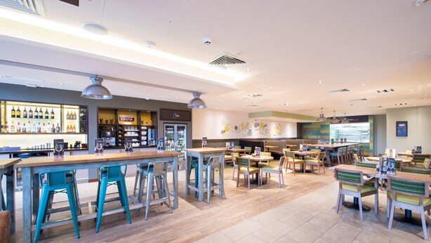 A spacious cafe with a bar area, multiple seating options, and a visible menu board. - Premier Inn Basingstoke Town Centre (Basingstoke)