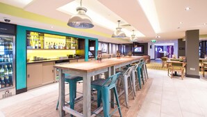 A bar area with a long counter, bar stools, and a television screen.