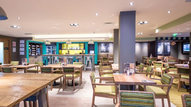 A restaurant with wooden tables and chairs, a bar area, and a television screen.