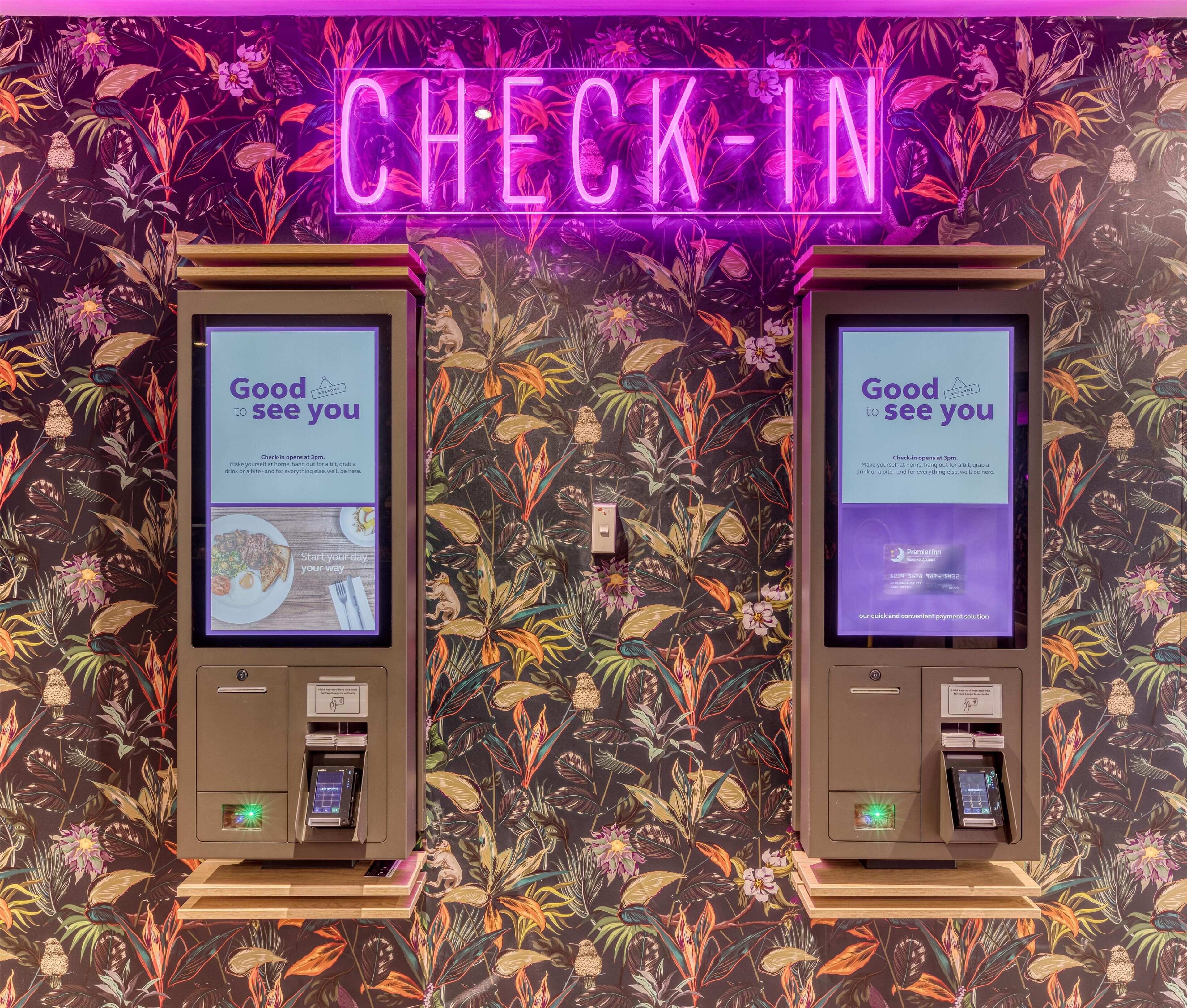 Dos quioscos de auto-registro con pantallas mostrando información del registro, sobre un fondo de papel tapiz floral.