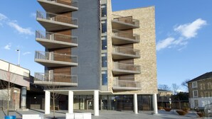 Un immeuble moderne à plusieurs étages, doté de balcons, d’une entrée imposante et surplombant un ciel dégagé.
