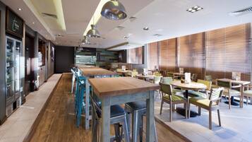 Un restaurant avec des tables hautes et des tabourets de bar, un plancher en bois et de grandes fenêtres équipées de stores.