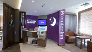 Un espace d’accueil d’hôtel comprenant un ordinateur, un kiosque en libre-service et un coin salon avec un canapé et une table.