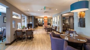 A hotel lobby with multiple dining areas, a reception desk, and a large vase with dried plants. - Premier Inn London Brentford (Brentford)