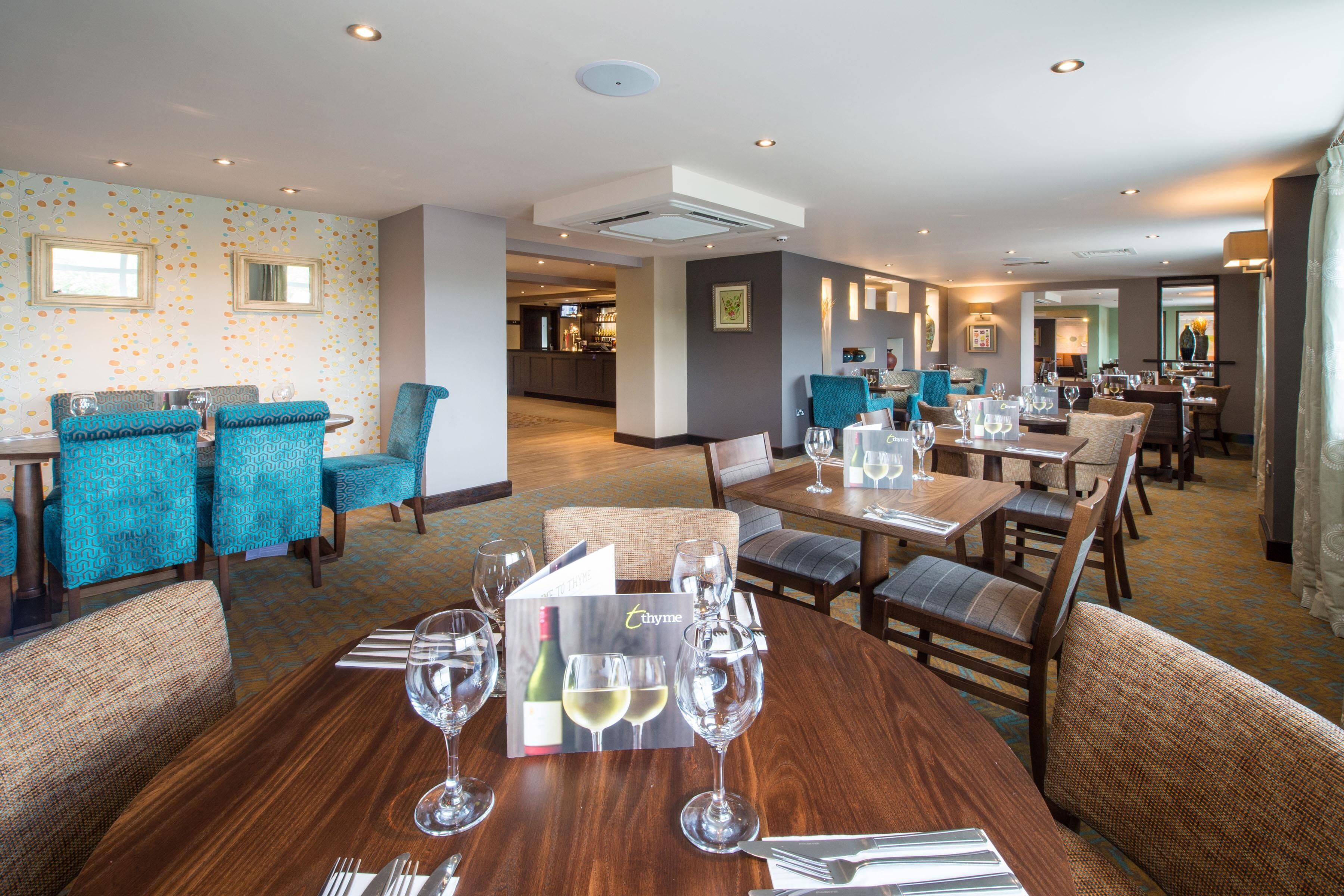 A hotel dining area with round tables, chairs, and a bar in the background.