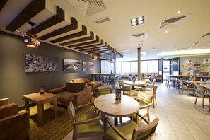 A modern restaurant with wooden furniture, round tables, and a high ceiling with geometric patterns. - Premier Inn St Andrews (St. Andrews)