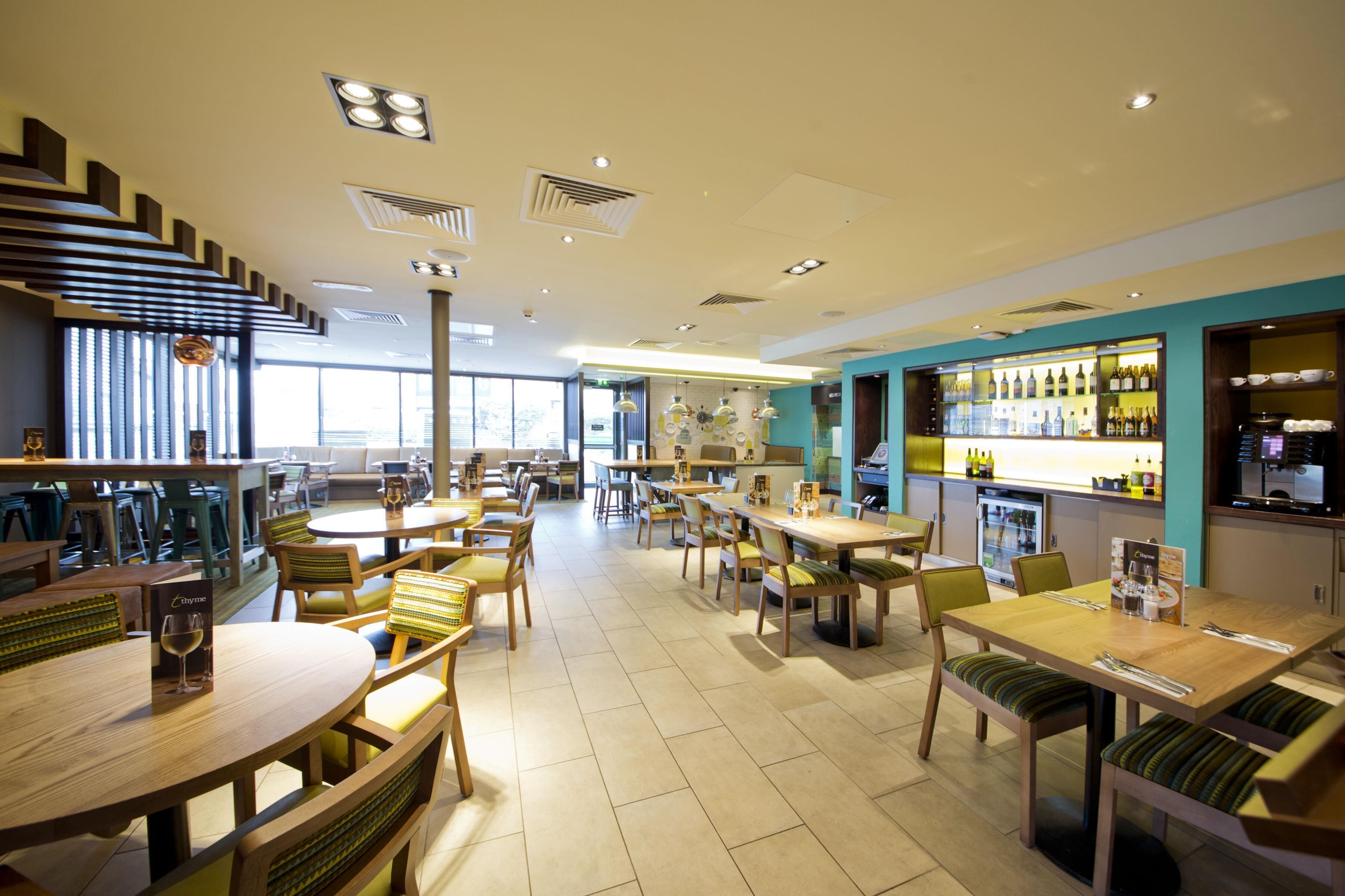 A spacious restaurant with multiple dining tables and chairs, a bar area with bottles, and a staircase leading to an upper level.
