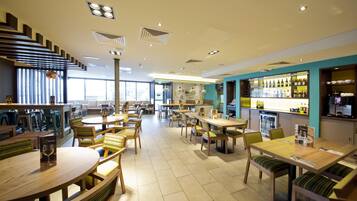 A spacious restaurant with multiple dining tables and chairs, a bar area with bottles, and a staircase leading to an upper level.