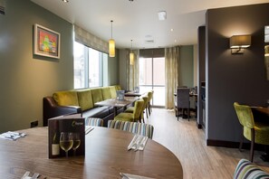 A hotel room with a dining area, a sofa, and a table set for two. - Premier Inn Sunderland City Centre (Sunderland)