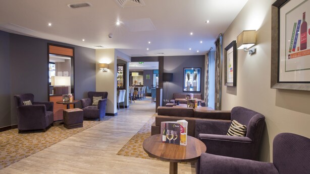 Eine Hotelhalle mit Sitzbereichen, einem Empfangsbereich und einer Bar/Lounge im Hintergrund.