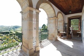 A balcony with stone columns, a wrought iron railing, and a view of a green landscape. - Parador Casa da Insua (Penalva Do Castelo)