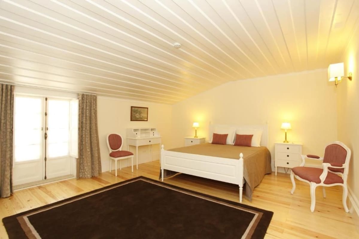 A bedroom with a bed, bedside tables, a chair, a desk, and a window with curtains.