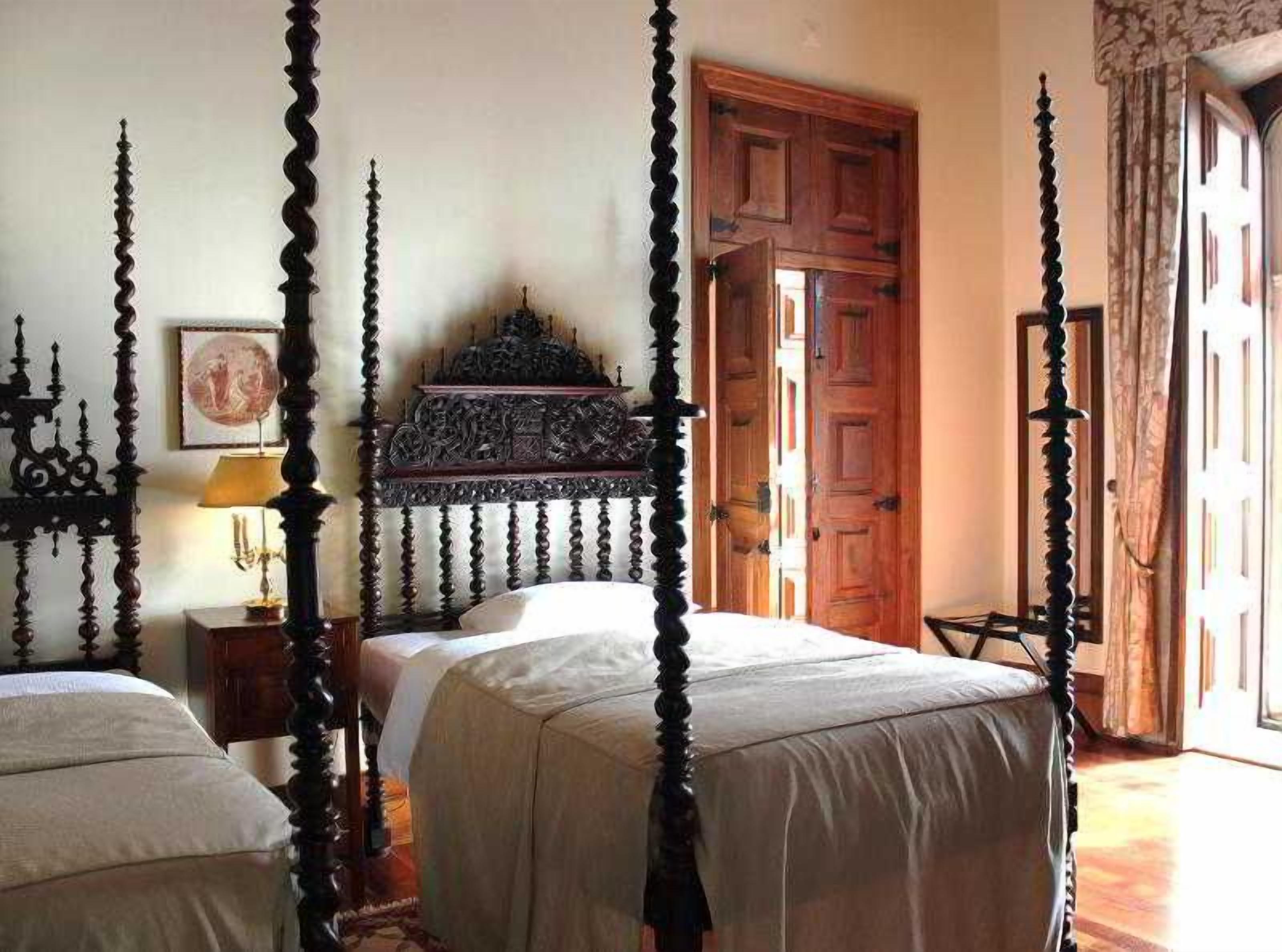 A bedroom with four beds, a wooden headboard, a nightstand with a lamp, and a door leading to another room.
