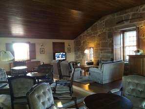 A cozy living room with stone walls, a television, comfortable seating, and a fireplace. - Parador Casa da Insua (Penalva Do Castelo)