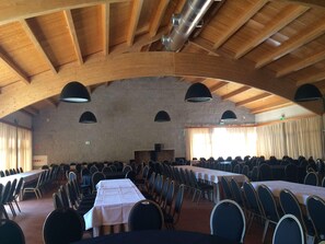 A large hall with high wooden ceilings, multiple tables with chairs, and a stage at the front. - Parador Casa da Insua (Penalva Do Castelo)