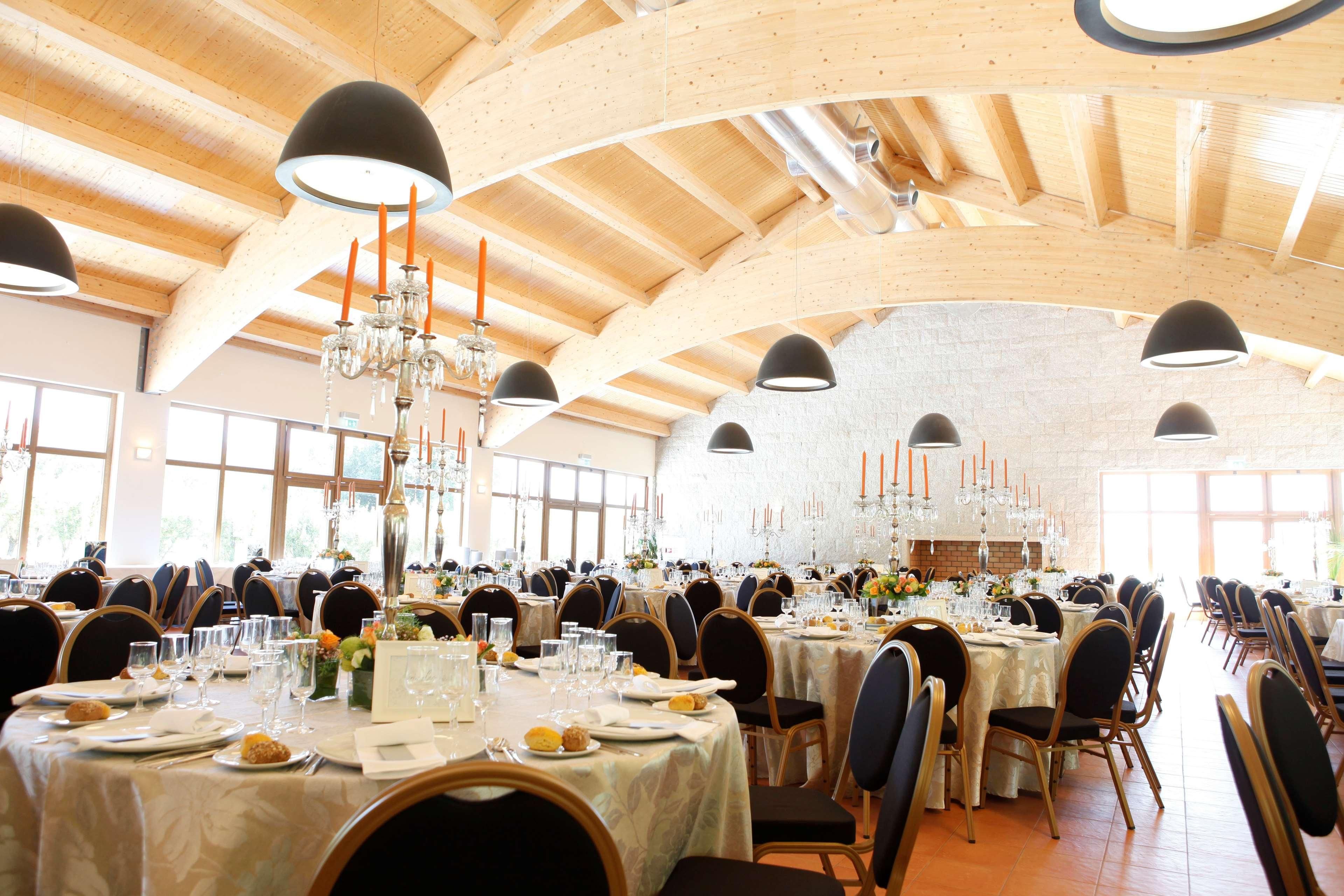 A large banquet hall with high wooden ceilings, multiple tables set for dining, and chandeliers.