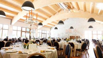 A large banquet hall with high wooden ceilings, multiple tables set for dining, and chandeliers.