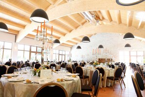 Une vaste salle de banquet avec de hauts plafonds en bois, de nombreuses tables dressées pour le repas et des lustres.