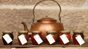 A copper teapot with a handle and spout, surrounded by four jars of honey with green lids and tags. - Parador Casa da Insua (Penalva Do Castelo)