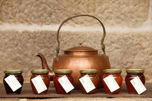 A copper teapot with a handle and spout, surrounded by four jars of honey with green lids and tags. - Parador Casa da Insua (Penalva Do Castelo)
