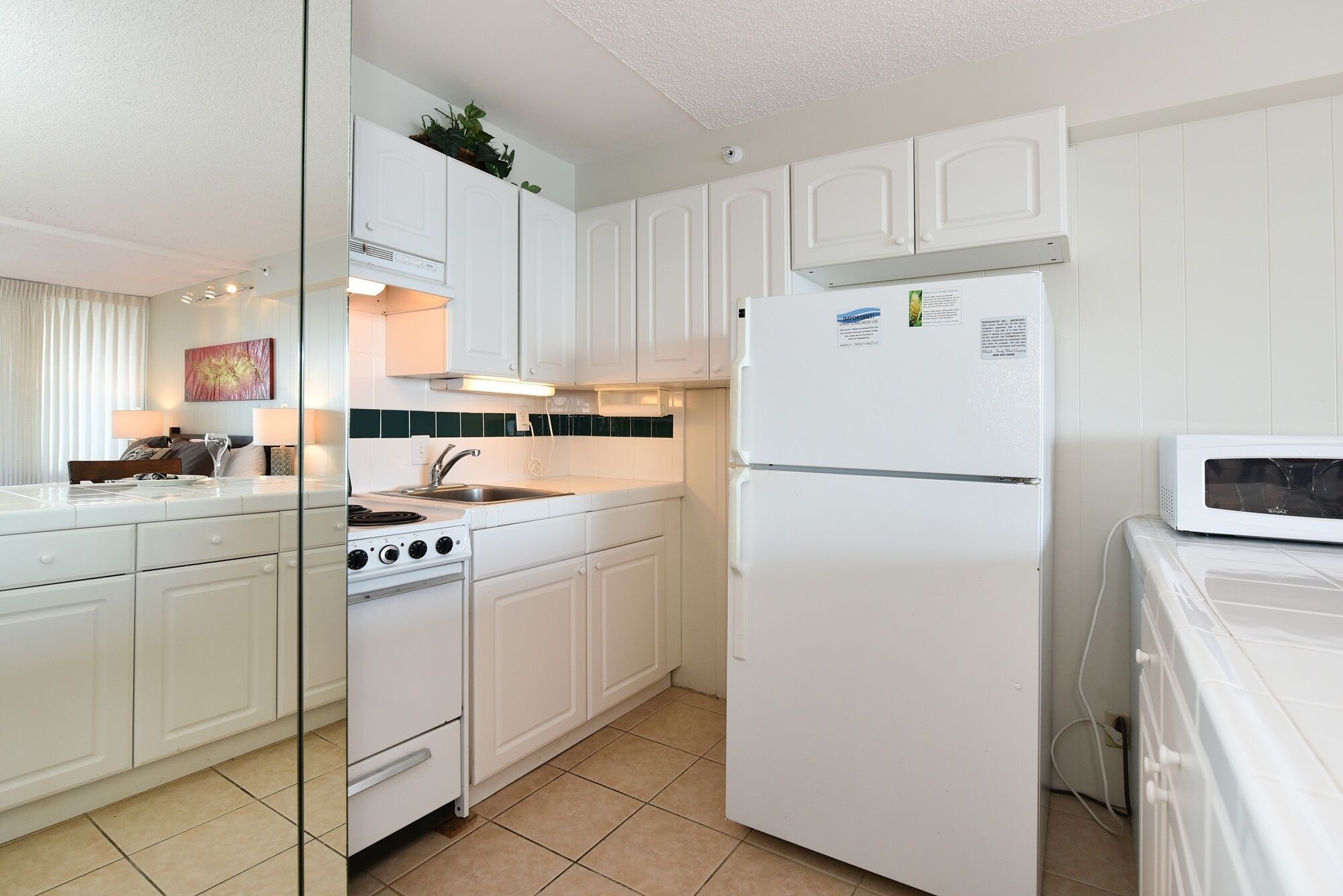 A compact kitchen with white cabinetry, a built-in stove, a refrigerator, and a microwave.