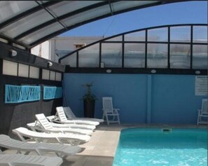 A covered swimming pool area with lounge chairs and a glass enclosure. - Hotel Rex Piriapolis (Piriapolis)