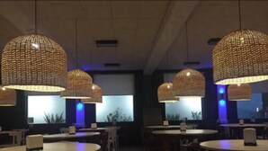 Un restaurante con mesas y sillas redondas, grandes lámparas colgantes de tejido y vistas al exterior a través de amplios ventanales.