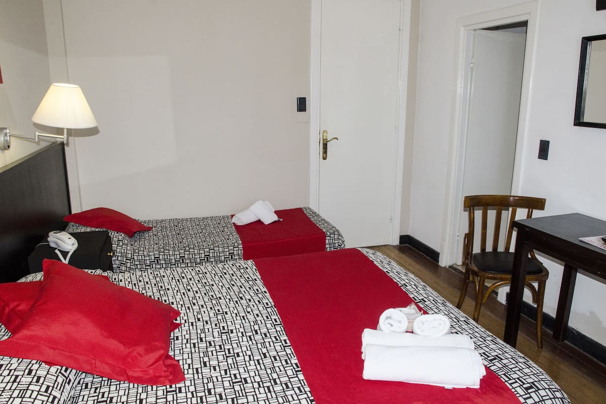 A hotel room with two beds, a desk, a chair, a lamp, and a door.