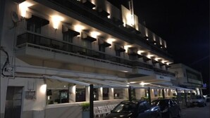 Un hotel de varios pisos con terraza al aire libre y coches estacionados frente a él.