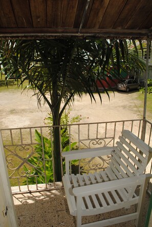 A covered outdoor seating area with a bench, a metal railing, and a palm tree.