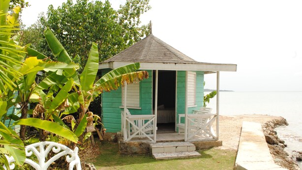 A small, single-story structure with a porch and a bench, situated near a body of water. - Bluefields on the Bay (Bluefields)