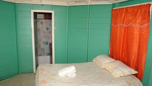 A room with teal walls, a bed with floral bedding, and an orange curtain. - Bluefields on the Bay (Bluefields)