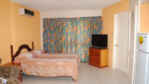 Um quarto com cama, cômoda, televisão e refrigerador.