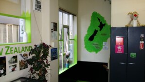 A room with a map of New Zealand on the wall, a refrigerator with stickers, and a window with blinds. - Backpackers Central Hamilton (Hamilton)