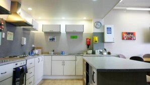 A modern kitchen with white cabinets, a stove, and a sink. There is a clock on the wall and a painting above the counter. - Backpackers Central Hamilton (Hamilton)