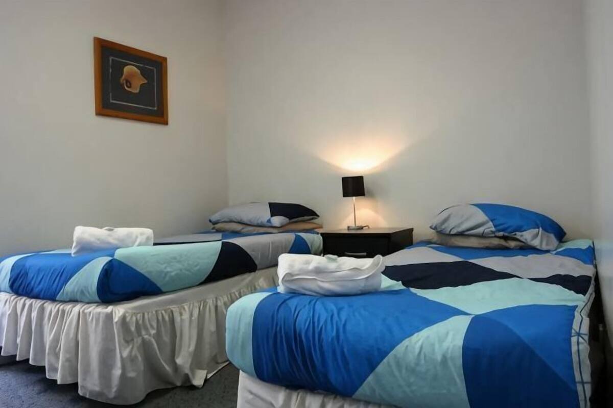 Quarto com duas camas, uma mesa de cabeceira com abajur e um quadro pendurado na parede.