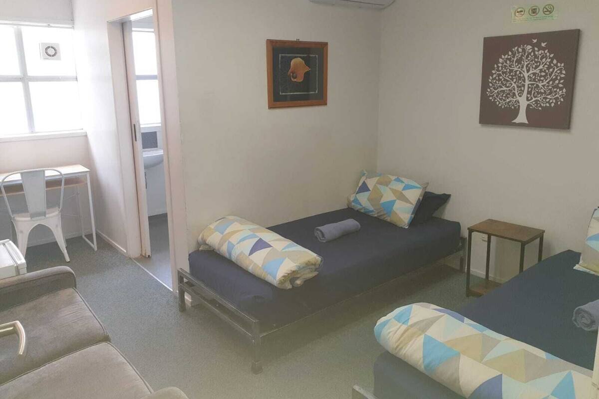 Quarto pequeno com uma cama de solteiro, escrivaninha, cadeira e ar-condicionado fixado na parede.