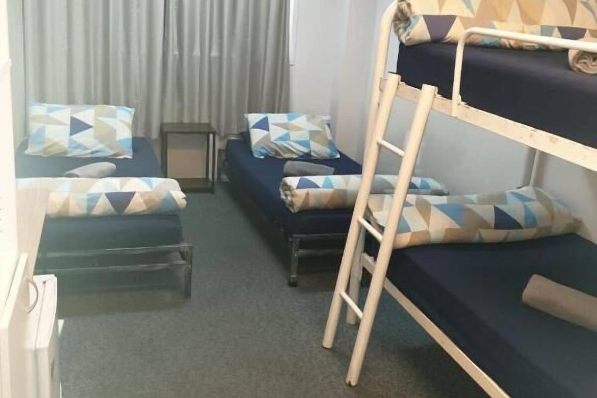Um quarto de dormitório com beliches, duas camas de solteiro, uma escrivaninha e uma cadeira.