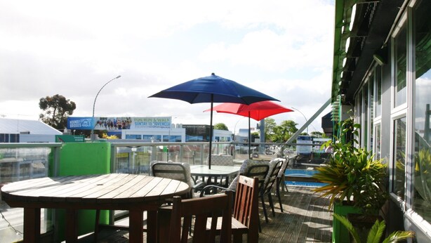 An outdoor patio with wooden tables and chairs, umbrellas, and a view of the cityscape. - Backpackers Central Hamilton (Hamilton)