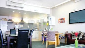 A modern hotel room with a dining area, kitchenette, and a flat-screen TV. - Backpackers Central Hamilton (Hamilton)