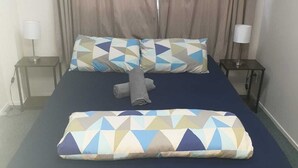 A neatly made bed with patterned pillows, a folded towel, and two bedside lamps on small tables. - Backpackers Central Hamilton (Hamilton)