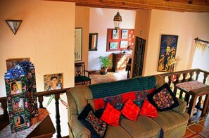 A cozy living area with a sofa, cushions, a staircase, and various artworks on the walls.
