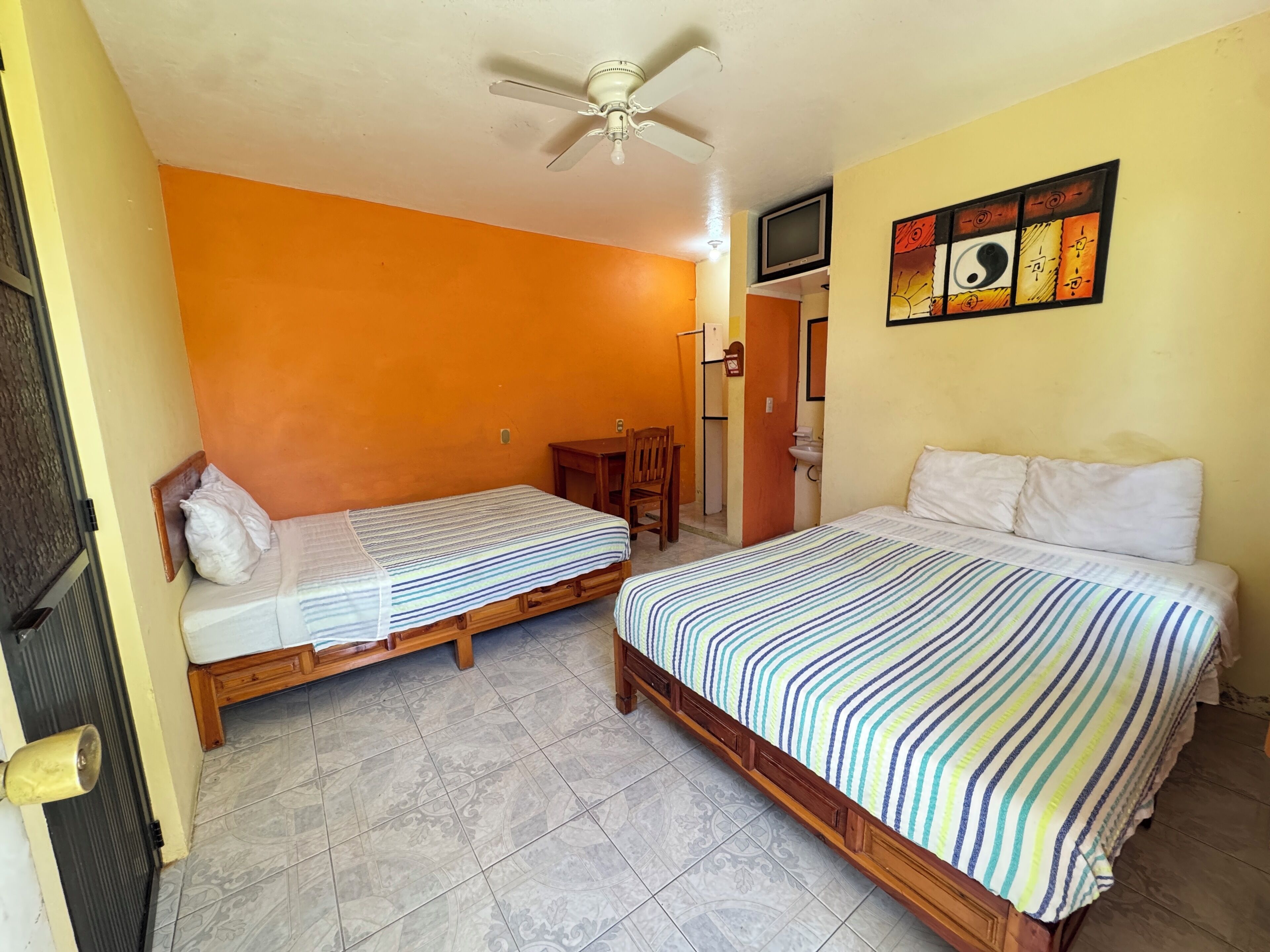 A room with two beds, a ceiling fan, a television, and a wall with artwork.