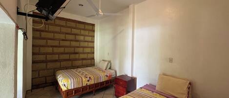 A bedroom with two beds, a ceiling fan, a brick wall, and a tiled floor.