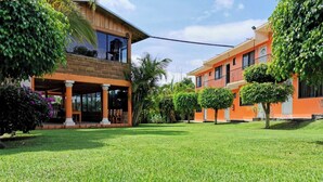 Un edificio de dos plantas con un patio cubierto, rodeado de césped cuidado y árboles pequeños.