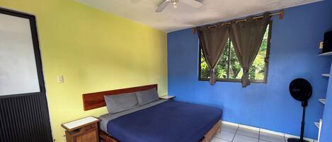 A bedroom with a wooden bed, a nightstand, a ceiling fan, a window with curtains, and a black speaker.
