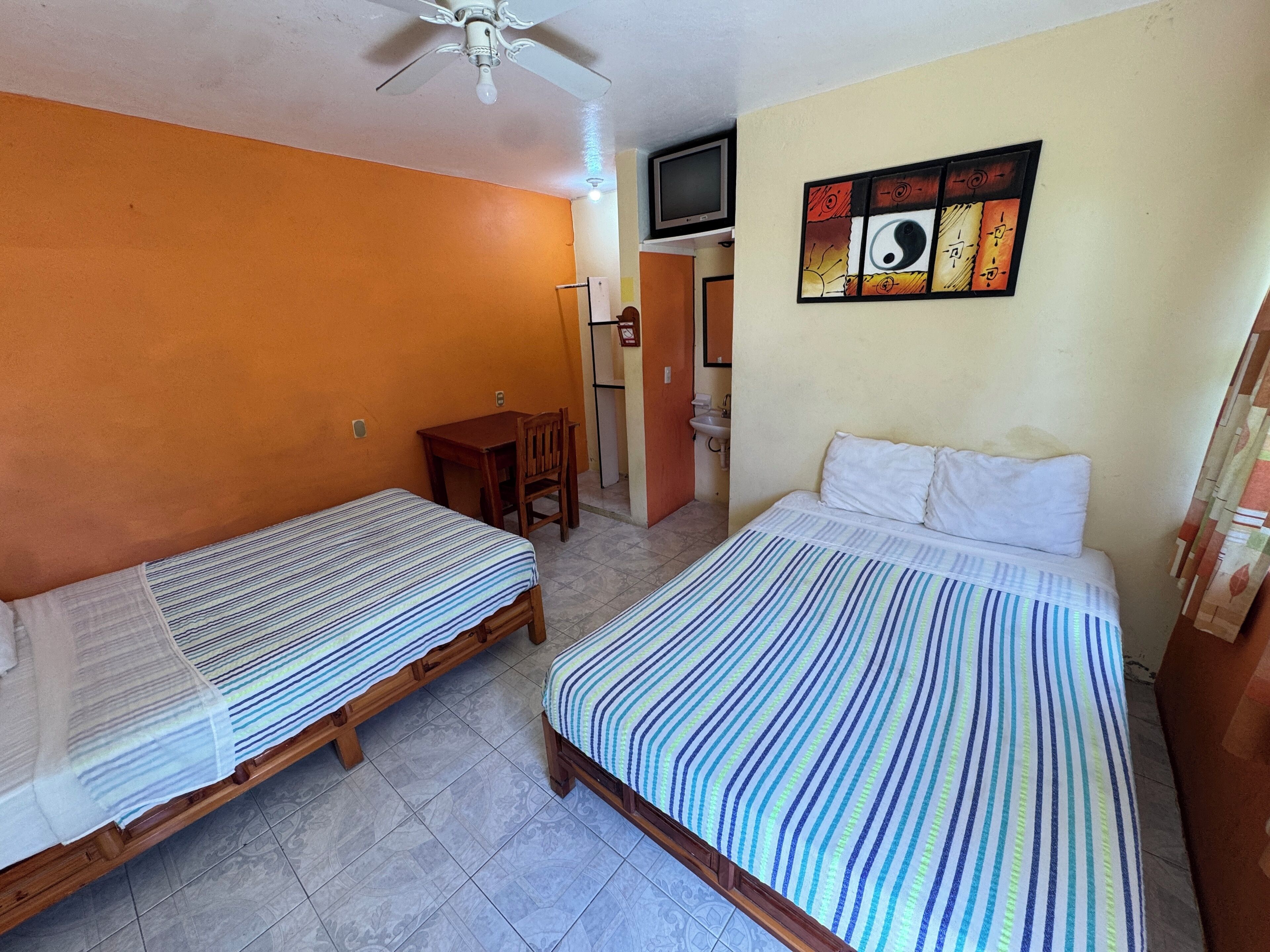 A room with two single beds, a desk, a chair, a television, and a bathroom.